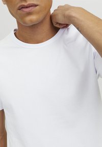White cotton T-shirt with a round neck and short sleeves, featuring a smooth texture and a relaxed fit. Close-up view of the neckline.