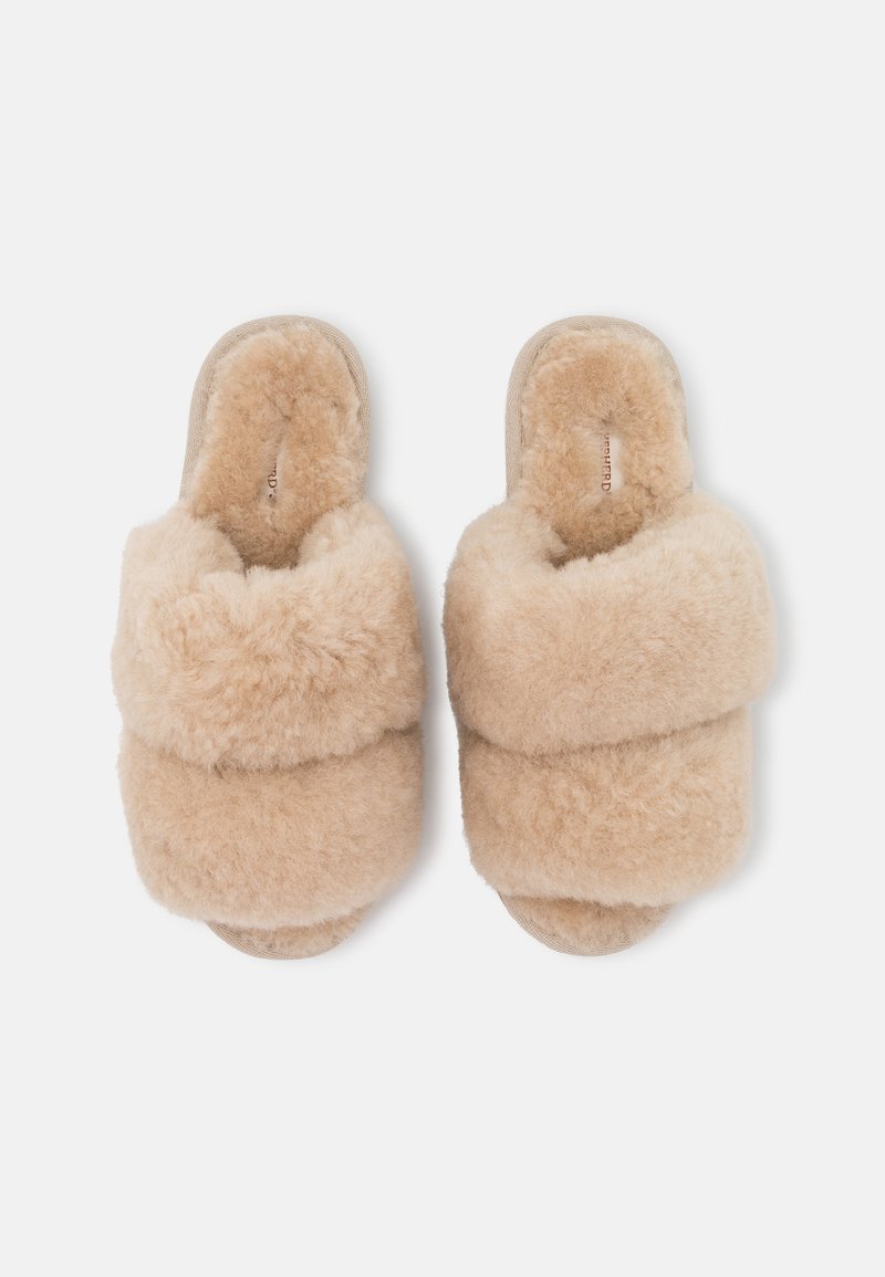Beige Fellpantoffeln mit zwei breiten, überlappenden Bändern. Weiche, flauschige Textur, offenes Zehen-Design und flache Sohle für Komfort.
