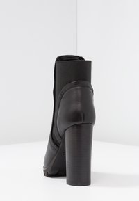 Botte de cheville en cuir noir avec un panneau élastique texturé, un bout arrondi et un talon haut cylindrique. Fini lisse et design minimaliste.