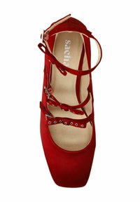 Chaussure en daim rouge avec un bout carré plat, plusieurs brides autour de la cheville et des éléments décoratifs. L'intérieur est beige avec une marque.