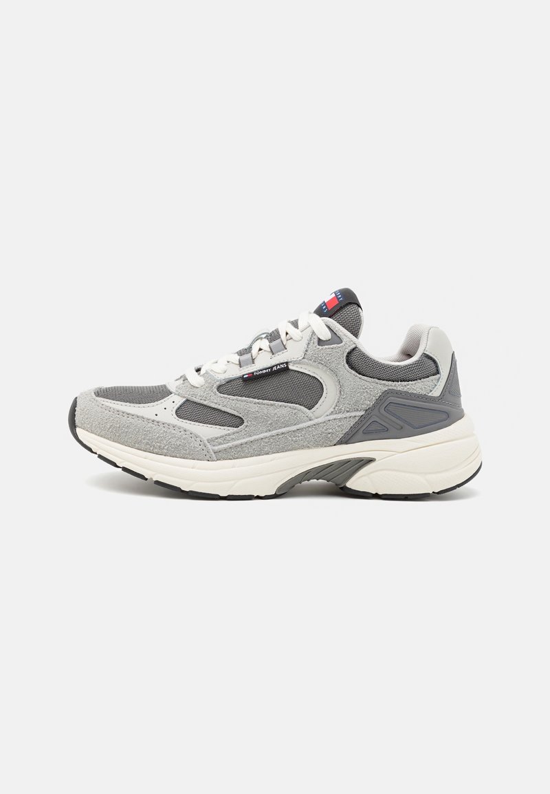Baskets de sport grises et blanches avec des panneaux en mesh et en daim, des lacets blancs et une semelle épaisse, avec un petit logo Tommy Jeans sur le côté.