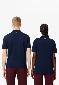 Granatowe koszulki polo z krótkimi rękawami, prążkowanymi kołnierzykami i zielonym logo z tyłu; w zestawieniu z bordowymi spodniami.