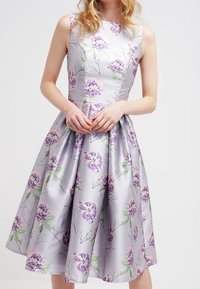 Kukallinen painettu mekko vaalean lilassa satiinissa, hihaton, istuva bodice ja liehuva hame, jossa on vihreät lehtikoristeet.