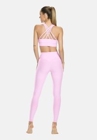 Rózsaszín sportmelltartó keresztbe fűzött pántokkal és hozzáillő, magas derekú leggings, sima, rugalmas anyagból készült. Feszes fazonnal rendelkezik.