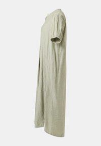 Robe vert clair à manches courtes, ample, avec une texture froissée, vue de profil sur un fond uni.