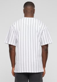 Mand iført en hvid kortærmet T-shirt med tynde sorte vertikale striber, vist fra ryggen mod en ensfarvet grå baggrund.