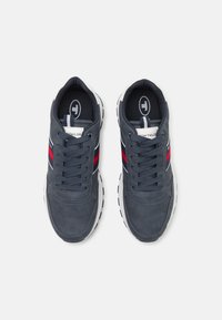 Baskets de sport bleu marine avec une tige en mesh, semelle intermédiaire blanche et accents rayés rouges et blancs. Elles disposent d'un système de laçage et d'une texture perforée.
