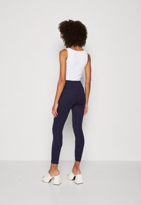 Hoge taille marineblauwe leggings van rekbare stof, met een slank ontwerp en gecombineerd met witte blockhak muiltjes.