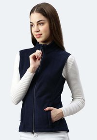 Marineblaue Fleece-Weste mit hohem Kragen, Reißverschluss und seitlichen Taschen, kombiniert mit einem weißen, gerippten Langarmoberteil. Glatte Textur und minimalistisches Design.
