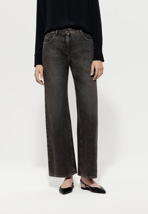 Vaqueros de pierna ancha, de color gris oscuro y tejido denim, con cintura alta, bolsillos delanteros y detalles sutiles de costuras. Combinados con zapatos planos negros.