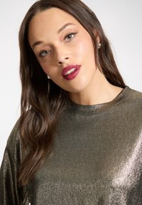 Metalicznie zielona bluzka z długim rękawem i okrągłym dekoltem, wykonana z fakturowanej tkaniny odbijającej światło, o luźnym kroju.