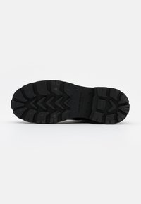 Semelle extérieure en caoutchouc noir avec des rainures profondes, présentant des motifs angulaires pour la traction. Nom de la marque embossé près du talon pour un détail supplémentaire.