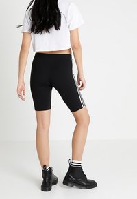 Black biker shorts with white side stripes, made from a stretchy material. Worn with a cropped white t-shirt and black ankle boots.