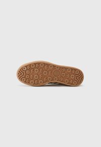 Semelle de chaussure en caoutchouc texturé beige, avec des motifs circulaires et des détails en vagues. Logo Adidas estampé au centre.