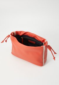Bolso de mano de cuero color coral con acabado texturizado, cierre de cremallera y costuras en blanco contrastante. El interior cuenta con un forro de tela oscura y un bolsillo.