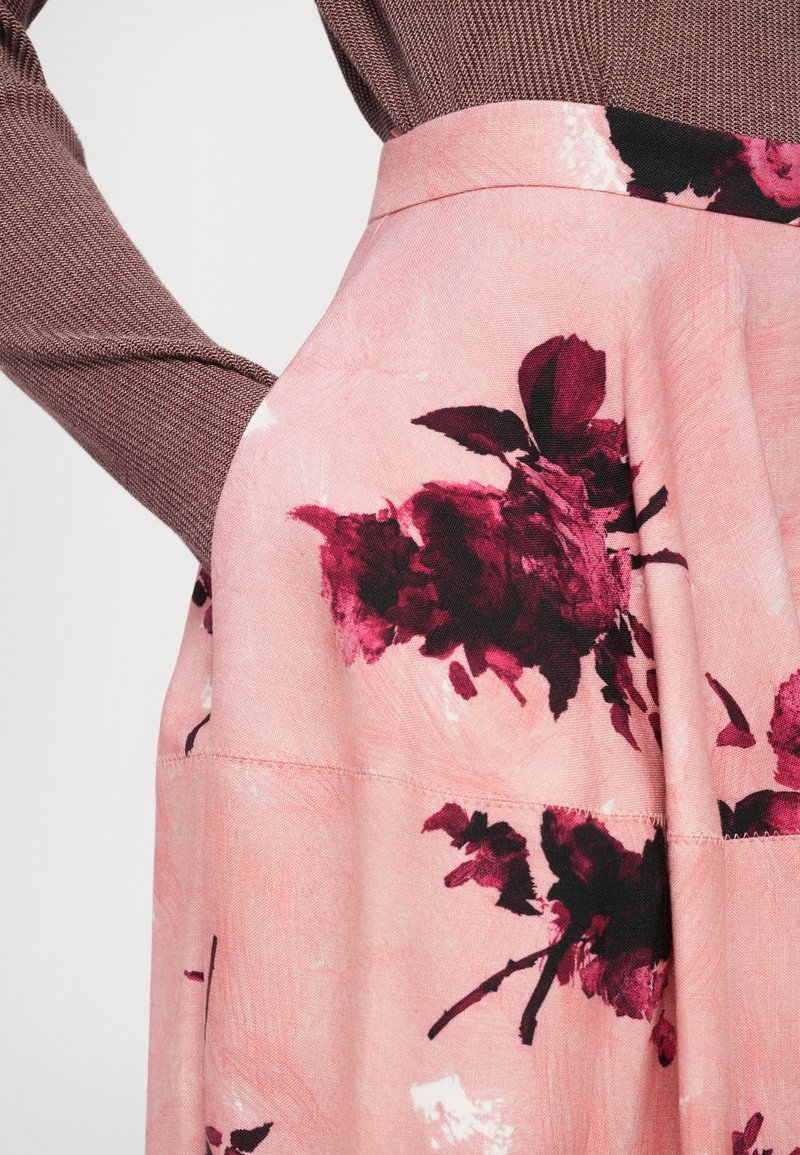 Blommig kjol i mjuk rosa tyg med stora mörkröda och svarta rosor, med en figursydd midja och flytande silhuett.