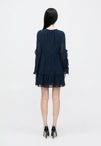 Φόρεμα από φιμέ σιφόν σε ναυτικό μπλε χρώμα με μακριά μανίκια, στρώσεις βολάν στο τελείωμα και τις μανσέτες, και κρυφό φερμουάρ στην πλάτη. Λείο υλικό και ελαφρύ σχέδιο.