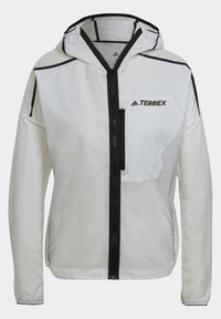 Veste légère blanche Adidas Terrex avec capuche, fermeture éclair noire à l'avant, poche poitrine et détails de coutures noires sur les manches et les épaules.