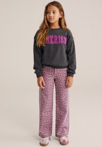 Szürke pulóver "CHERISH" felirattal pink textúrált betűkkel, párosítva rózsaszín leopárdmintás bőnadrággal és rózsaszín sportcipővel.