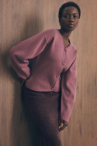 Vijoličasti kardigan iz mešanice volne z dolgimi rokavi, okroglo izrezom in gumbi. Usklajen s temno teksturirano krilom do kolen.