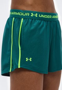 Τζελ αθλητικό σορτς Under Armour με νέον πράσινη ραφή και λογότυπο, φορεμένο από άτομο με ορατό πάνω μηρό και μέση.