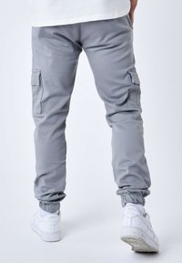 Pantalones cargo grises con puños elásticos, bolsillos laterales y una textura suave, combinados con zapatillas blancas que tienen un logo en el talón.