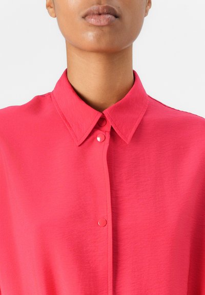 Blouse rose avec un col structuré, dotée d'une fermeture à boutons classique et d'une texture de tissu lisse et léger.