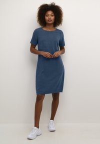 Short-sleeve, knee-length dress in a solid dark blue fabric. Features a round neckline and side pockets. Paired with white sneakers.