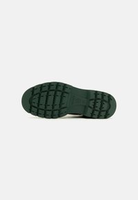 Semelle de chaussure en caoutchouc verte avec un motif de semelle texturé. Comprend des découpes circulaires et ovales pour une meilleure adhérence et flexibilité.
