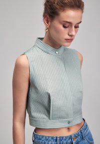Blusa sin mangas de color azul claro, corta, con rayas verticales, cuello alto y cierre de botones en la parte delantera y en el dobladillo.