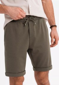 Olivgröna shorts med texturerat tyg, elastisk midja och justerbar dragsko. Har uppvikta fållar och sidofickor.