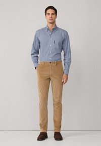 Camisa a cuadros en azul claro y blanco, pantalones de pana marrones y zapatos marrones oscuros. La camisa tiene un cuello con botones y un pequeño bolsillo.