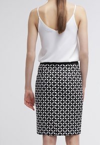 White sleeveless top paired with a black and white patterned pencil skirt featuring geometric shapes. Smooth fabric with a fitted design.