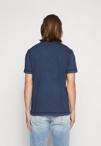 Μπλέ ναυτικού μπλουζάκι από βαμβάκι, κοντά μανίκια, στρογγυλή λαιμόκοψη, με ορατές ραφές, φορεμένο με ανοιχτό μπλε ξεθωριασμένα τζιν.