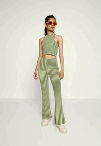 Conjunto de top cropped às riscas verde e amarelo e calças flared, feito de tecido elástico. Combinado com óculos de sol laranja e sapatos de plataforma brancos e grossos.