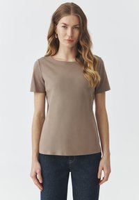 Top a maniche corte di un morbido color taupe, con scollatura rotonda e una texture liscia. Abbinato a jeans in denim scuro.