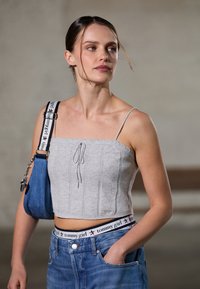 Grå kort strikket topp med et teksturert mønster, justerbare stropper og snøring foran. Kombinert med lyseblå høyhalsede jeans med merkevarebelte.