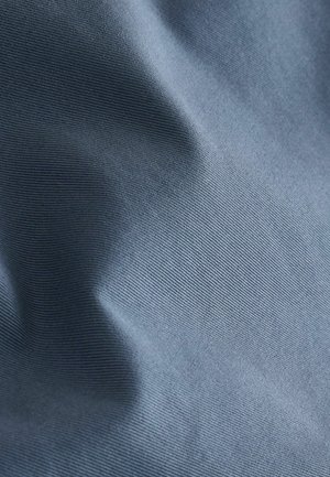 Hellblaues Stoffmaterial mit feiner horizontaler Textur und weichen Falten, die subtile Schatten und Lichtreflexe erzeugen.