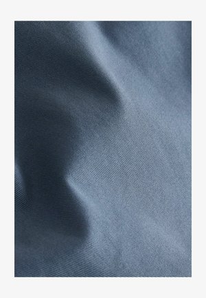 Hellblaues Stoffmaterial mit feiner horizontaler Textur und weichen Falten, die subtile Schatten und Lichtreflexe erzeugen.