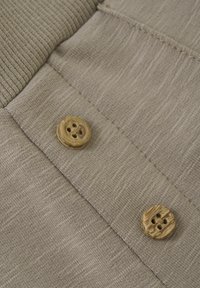 Beige stickad tyg med en mjuk textur har två runda träknappar med fyra hål, placerade på en vikt kant.