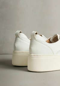 Pantofi sport albi din piele cu finisaj texturat, având o talpă groasă bej și detalii subtile de cusături lângă călcâi.