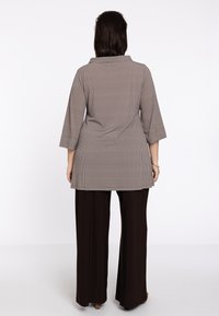 Geverifieerde tuniek met een brede kraag, driekwartmouwen en een losse pasvorm; gecombineerd met donkerbruine wijde broek.