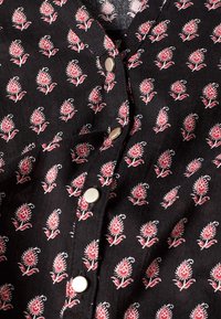 Schwarzer Stoff mit kleinen roten und weißen Blumenmustern und vier sichtbaren silbernen runden Knöpfen entlang der mittleren Naht.