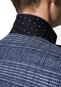 Marynarka z kołnierzykiem, wykonana z fakturowanej granatowej tkaniny w kratkę, z kontrastowym czarnym kołnierzem ozdobionym białymi kwiatowymi kropkami.