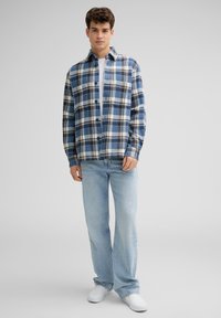Gekleed in een geruite shirt met blauw, zwart en witte kleuren, met knoopsluiting en een kraag. Gecombineerd met lichtblauwe jeans en witte schoenen.