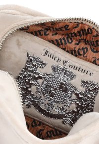 Interno beige in peluche con emblema argento che presenta due cani stilizzati, una corona dettagliata e la dicitura "Juicy Couture" incisa sulla fodera in tessuto color beige.