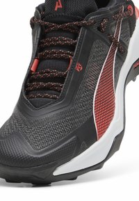 Scarpa da atletica nera con tomaia in mesh testurizzato, dettagli rossi, colletto imbottito e sistema di allacciatura tradizionale. Caratterizzata da una suola esterna in gomma resistente.