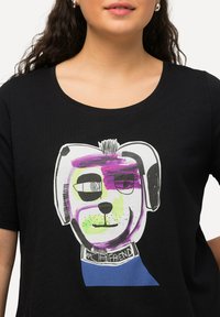 Černé tričko s barevnou grafikou karikaturního psa s abstraktními rysy a obojkem, na kterém je napsáno "MŮJ PŘÍTEL."