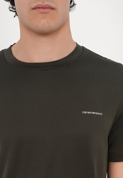 T-shirt en coton vert foncé avec un col rond, présentant un petit logo blanc "Emporio Armani" sur la poitrine gauche.