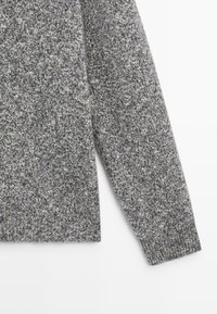 Maglione grigio lavorato a maglia con un motivo testurizzato, caratterizzato da un collo rotondo e maniche lunghe. I polsini e l'orlo sono a coste per un finish aderente.
